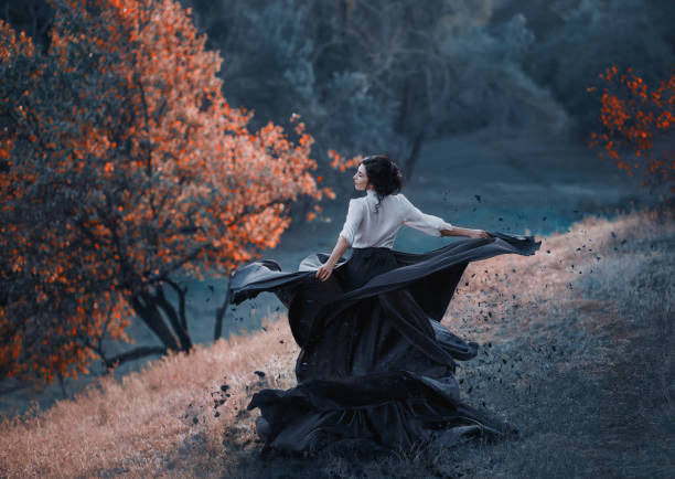 mysterious girl with dark hair and a long flying black vintage dress runs through the woods, a charming ambush, a great attractive witch turns into a crow, waving a train like bird wings - witch beauty beautiful women imagens e fotografias de stock