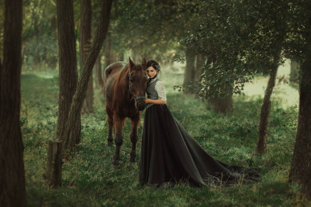 mysterious girl with dark hair and a long flying black vintage dress runs through the woods, a charming ambush, a great attractive witch turns into a crow, waving a train like bird wings Gourmet lady in a vintage dress. A beautiful rider gently hugs the horse. Artistic Photography white shirt black skirt stock pictures, royalty-free photos & images