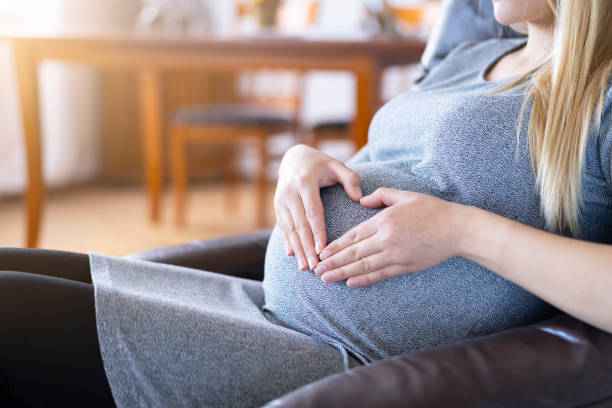 istock Pregnant woman sitting on sofa and making heart shape 1141014445