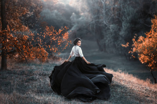 mysterious girl with dark hair and a long flying black vintage dress runs through the woods, a charming ambush, a great attractive witch turns into a crow, waving a train like bird wings A girl in a vintage dress is running and looking around. The train waving in the wind. Artistic Photography gothic fashion stock pictures, royalty-free photos & images
