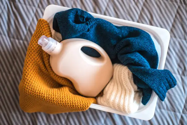 Photo of Bottle of detergent with sweaters in container.