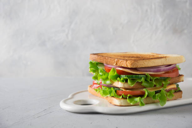istock Sandwich with white toast bread, bacon, tomato, onion, salad, cheese on light. Space for text. 1141019837