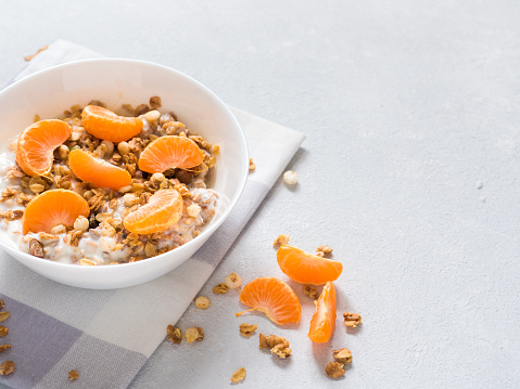 Healthy breakfast. Baked muesli with tropical fruits, fresh tangerines and yogurt on white background