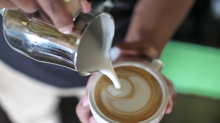 Close-up of Barista adding foamy milk into a cup of coffee