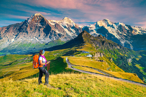 Famous Mannlichen tourist resort and cable car station. Backpacker hiker woman enjoying the view with high snowy mountains at sunset, Grindelwald, Bernese Oberland, Switzerland, Europe