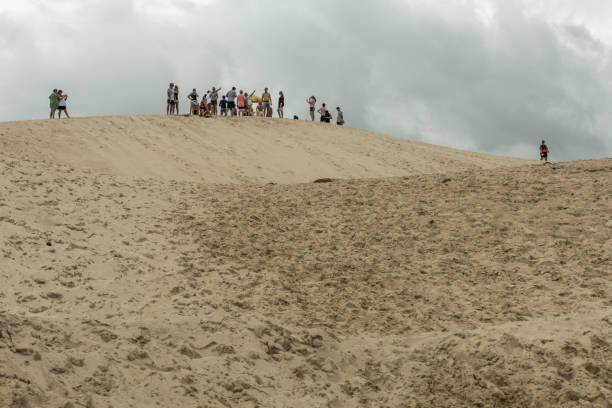 A group of people on the top of a sand mountain on a dunes area in Joaquina Beach, in Florianopolis, Brazil. 2019, January. Florianopolis, Brazil. A group of people on the top of a sand mountain on a dunes area in Joaquina Beach. joaquina beach in florianopolis santa catarina brazil stock pictures, royalty-free photos & images