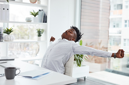 Shot of a young businessman stretching while working in an office