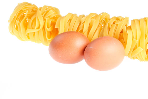 Raw dry tagliatelle noodle, eggs close up isolated on white background