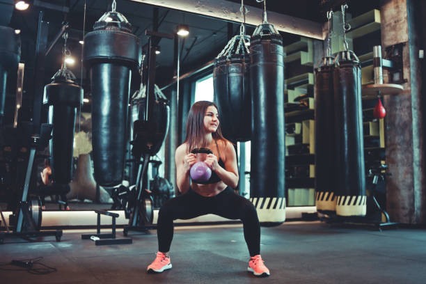 istock Functional training. Woman doing squats exercise with kettlebell indoors at gym 1141043018