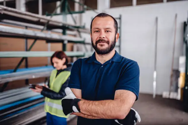 Portrait of warehouse worker looking at camera with female warehouse clerk standing behind him