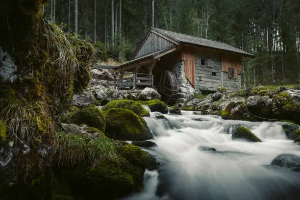 Idyllic long exposure view of an old abandoned mill with mossy rocks lying in beautiful riverbed in a mystic forest on a cloudy moody day in springtime, Golling, Salzburger Land, Austria