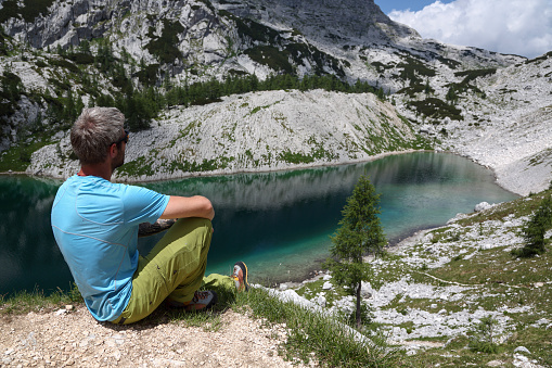 Mid-adult man sitting above a green mountain lake. Tranquil scene in mountains.