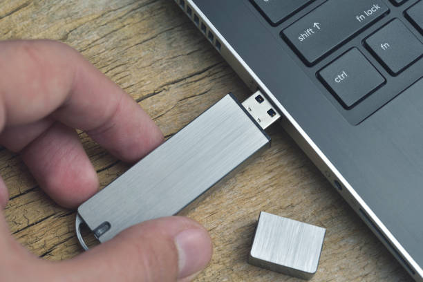 木製の机の上のラップトップに接続された金属製の usb フラッシュドライブのクローズアップ - disk media ストックフォトと画像