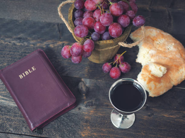 Man breaking the bread, with wine, grapes and Bible in the background stock photo