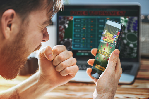 Lucky man celebrating victory after getting jackpot in online casino. Poker tournament on the laptop screen on the background.