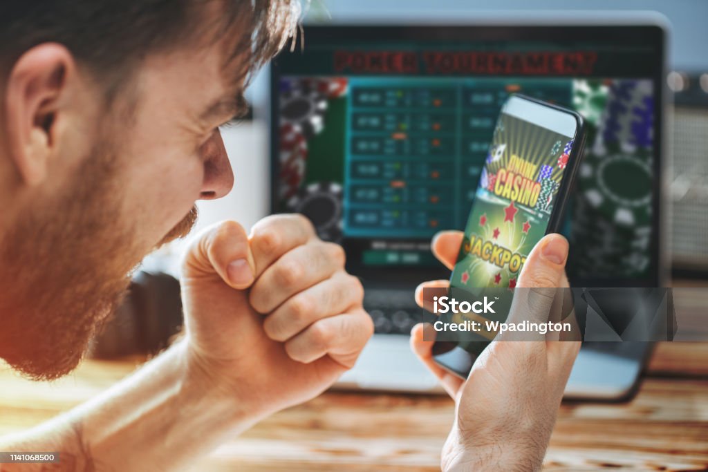 Man celebrating victory after making bets at bookmaker website Lucky man celebrating victory after getting jackpot in online casino. Poker tournament on the laptop screen on the background. Internet Stock Photo