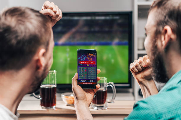 Two male friends watching live football game broadcast on tv Two male buddies watching live football game broadcast on tv and celebrating money win after making bets online at bookmakers website. gambling stock pictures, royalty-free photos & images