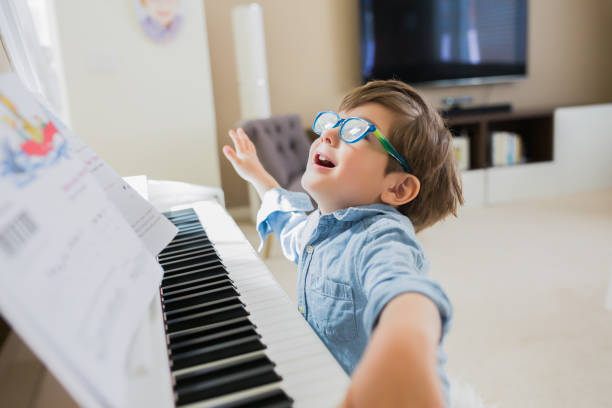 Preschool age boy with eyeglasses is playing a white piano.