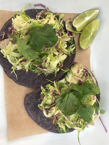 a pair of fresh gourmet tacos made with purple corn tortillas and fresh jalapenos, cilantro, meat and shredded vegetables