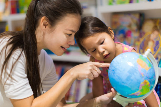 a teacher and a preschool student learning geography on a world globe - searching child curiosity discovery imagens e fotografias de stock