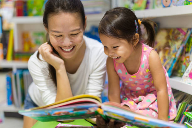 Parent and child reading books together in the library. Teacher reading a educational book to her female student, having a good time in class learning. reading stock pictures, royalty-free photos & images