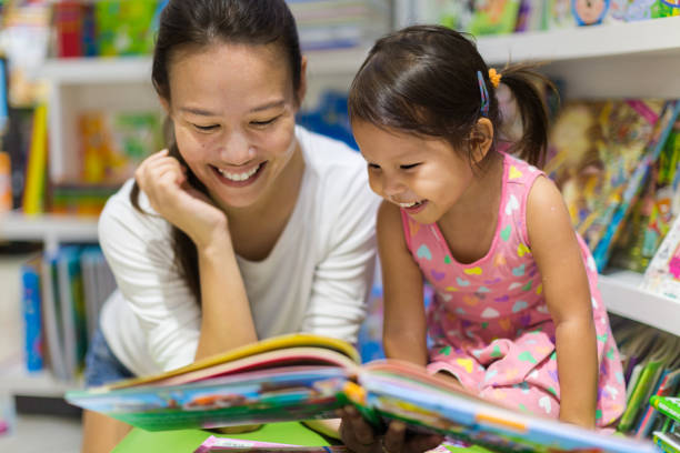 Parent and child reading books together in the library. Teacher reading a educational book to her female student, having a good time in class learning. parent and child reading stock pictures, royalty-free photos & images