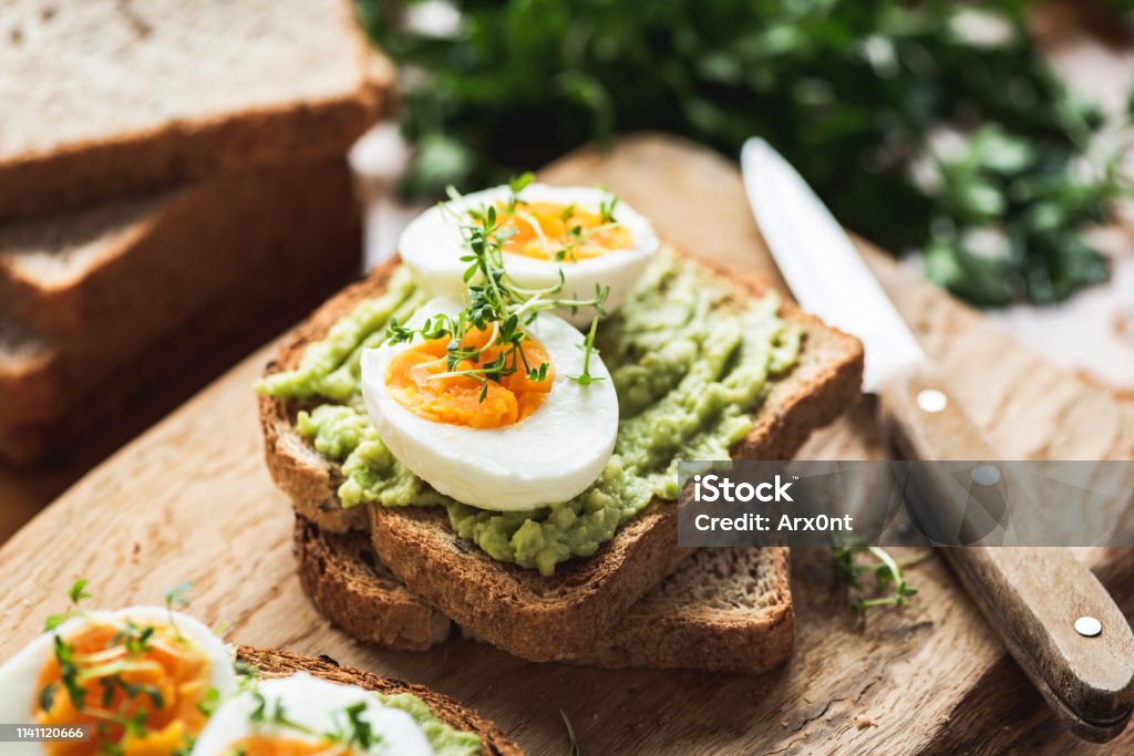 Healhy Breakfast Toast With Avocado, Egg Healhy Breakfast Toast With Avocado, Boiled Egg On Wooden Cutting Board Breakfast Stock Photo