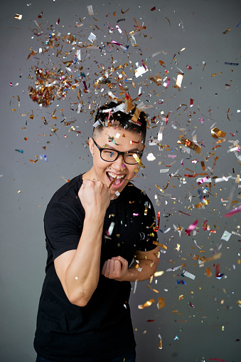 Portrait of happy successful young man standing under falling confetti