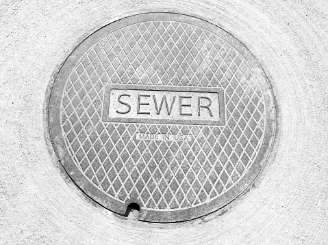 A sewer lid manhole cover on the street that says Sewer.