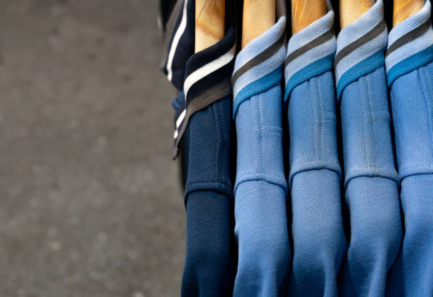 seitenansicht von mehreren lila blauen unisex-polo-shirts, die an holzbügeln an einem einzelhandelsmarkt hängen - horizontal gestreiften vorhängen stock-fotos und bilder