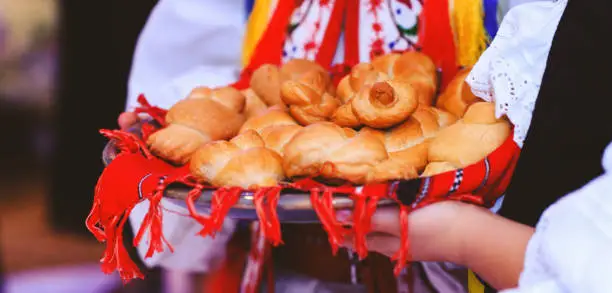 Baked buns or cakes in the hands of the children dressed in traditional costume. Bread in form of snails or pigeons in the red towel with elements of Romanian culture. Holiday scenic picture with tricolor national symbol of Romania and Moldova.