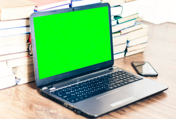 istock Green screen laptop, stack of books, smartphone, notebook and pencils on white table, education office concept background 1141142555