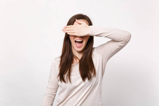 Portrait of cheerful young woman in light clothes covering eyes with hand keeping mouth open isolated on white wall background in studio. People sincere emotions lifestyle concept. Mock up copy space. Portrait of cheerful young woman in light clothes covering eyes with hand keeping mouth open isolated on white wall background in studio. People sincere emotions lifestyle concept. Mock up copy space hair covering eyes stock pictures, royalty-free photos & images
