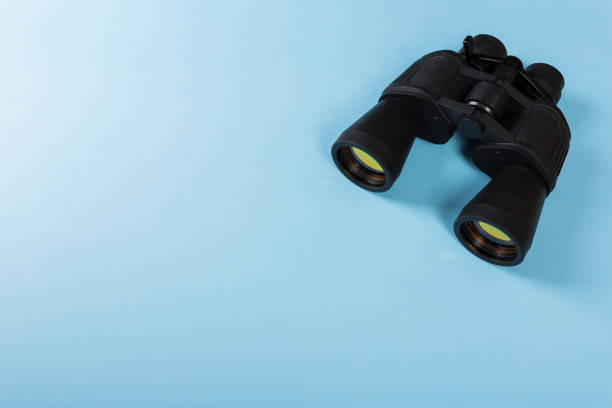 istock Black binoculars with orange lens on blue background 1141144130