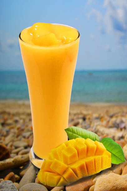 istock Mango smoothie in high glass served with slided mango isolated on seascape background. Mango shake shooting in studio. Image with path. Tropical fruit concept. 1141144879