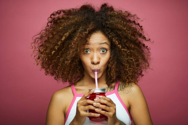 hermosa afro mujer joven caribeña en ropa de verano contra el fondo rosado. - drinking straw drinking juice women fotografías e imágenes de stock