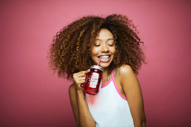 belle afro des caraïbes jeune femme en vêtements d’été contre fond rose. - juice drinking women drink photos et images de collection