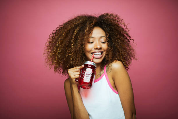 ピンクの背景に対する夏��の服の美しいアフロカリブ海の若い女性。 - smoothie drinking women drink ストックフォトと画像