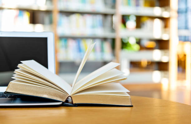 istock Laptop and open book on the table of public library 1141156200