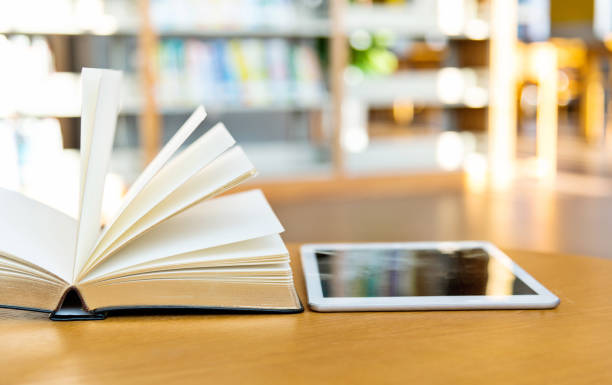 istock Digital tablet and open book on the table of public library 1141156410