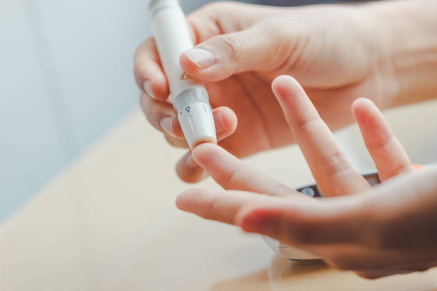 крупным планом руки женщины с помощью ланцет на пальце, чтобы проверить уровень сахара в крови глюкозы метр с помощью медицины - diabetes стоковые фото и изображения