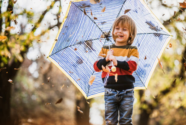 Cute happy boy having fun while holding umbrella in autumn day at the park.