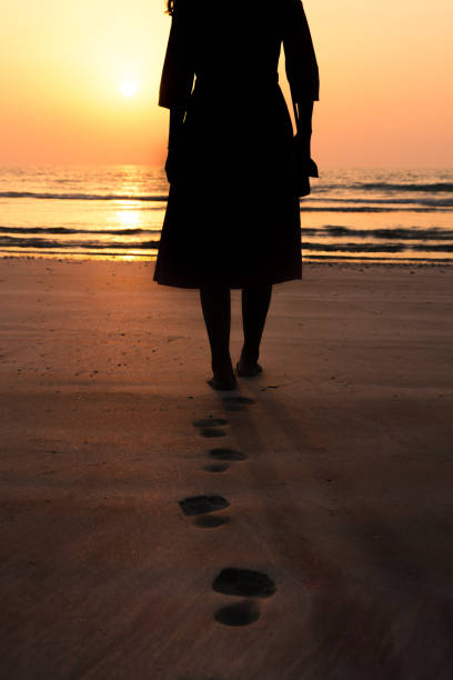 istock Woman walking towards seaside at sunset 1141165993