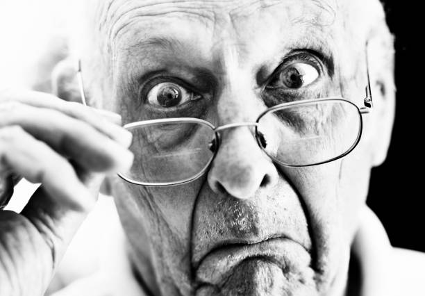 A horrified old man peers over his spectacles at the camera, shocked and disgusted by what he sees.