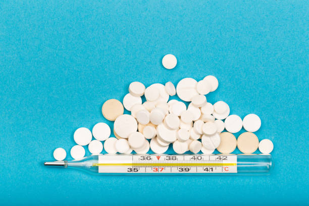 istock medical  thermometer and white pills on blue  background close up view- Image 1141180082