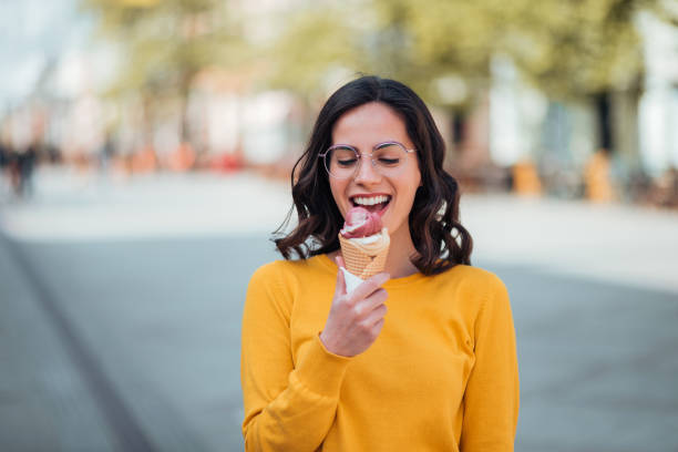 тысячелетняя женщина ест мороженое в весенний солнечный день. - frozen sweet food стоковые фото и изображения