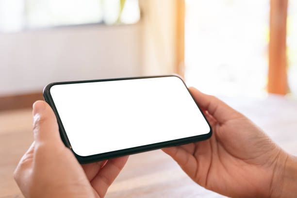 istock Mockup image of woman's hands holding black mobile phone with blank white screen horizontally on wooden table 1141180513
