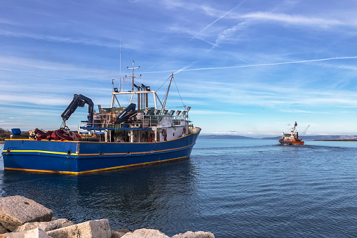 two fishing trawlers leave the port in early evening