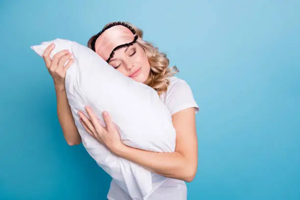 Close up photo beautiful funky her she lady hands arms palms hold cuddle big large pillow careless expression glad day off wear sleeping pink mask casual white t-shirt clothes isolated blue background.