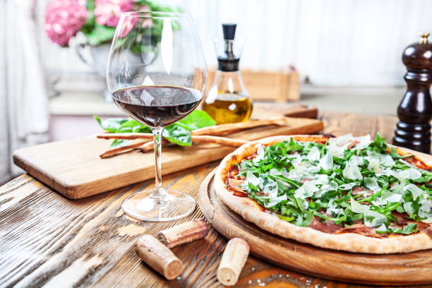 istock Close up view on fresh served pizza with prosciutto on a wooden table on light background. Pizza with wine. Vertical image with copy space for text. 1141185231